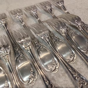 Op de afbeelding: Een verzameling sierlijke zilveren vorken. Elke vork heeft een gedetailleerd bloemmotief op de steel en tanden. Het bestek is in een close-up gerangschikt, waarbij de ingewikkelde patronen en de gepolijste afwerking worden getoond.