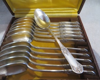 May include: A set of 10 silver teaspoons in a brown velvet-lined box. The spoons have ornate handles and are arranged in a row.