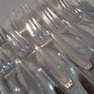 May include: A close-up of a set of silver forks with ornate designs. The forks are arranged in a row, with the tines pointing towards the viewer.