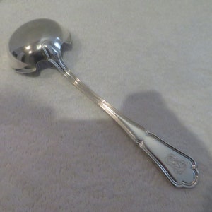 Puede incluir: Una cuchara de servir de plata con un mango decorativo y un monograma.