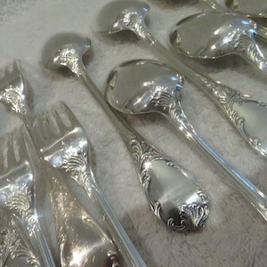 May include: A set of silver forks and spoons with ornate handles. The silverware is arranged in a row on a white surface.