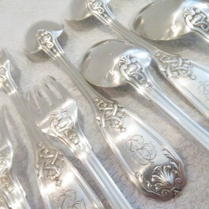 Puede incluir: Un juego de tenedores y cucharas de plata con mangos ornamentados. Los mangos presentan diseños intrincados y están decorados con un monograma.