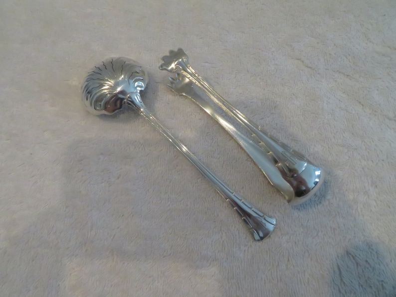 May include: A set of two silver serving utensils. One is a spoon with a decorative design and the other is a pair of tongs.
