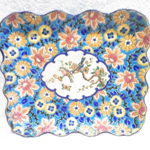 Peut inclure: Un plateau en céramique bleu et blanc avec un bord festonné. Le plateau est décoré d'un motif floral et de deux oiseaux sur une branche.