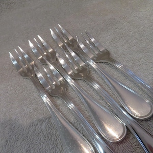 Peut inclure: Un ensemble de huit fourchettes en argent plaqué avec des manches ornés. Les fourchettes sont disposées en éventail, les pointes des dents pointant vers le centre.