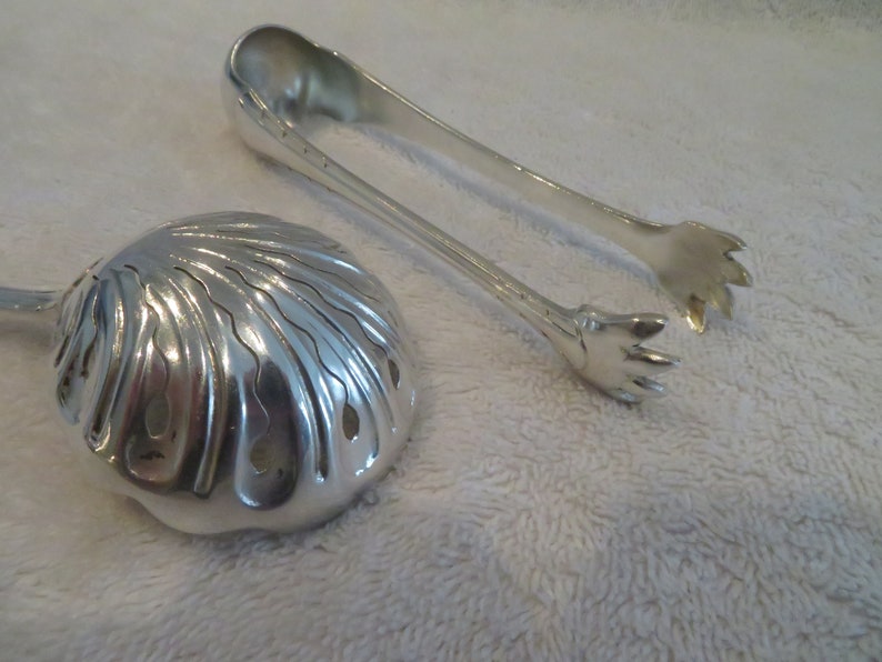 May include: Silver serving set with a shell-shaped serving spoon and a pair of tongs with claw-like ends.