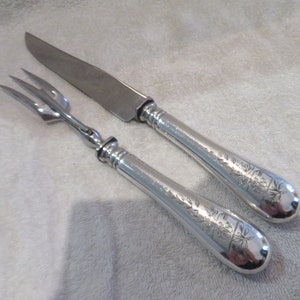 May include: A silver serving set with a knife and fork. Both pieces have ornate floral designs on the handles.
