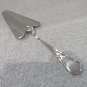 Peut inclure: Un serveur à gâteau en argent avec une poignée ornée et un bord festonné.