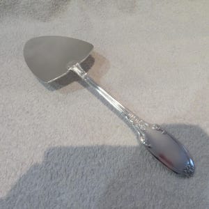 Puede incluir: Servidor de pastel de plata con un mango adornado y una hoja triangular.