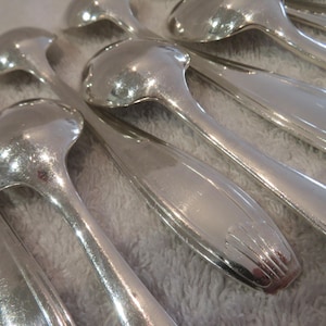 May include: A set of silver spoons with ornate handles. The spoons are arranged in a fan shape, with the handles overlapping.