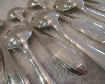 May include: A set of silver spoons with ornate handles. The spoons are arranged in a fan shape, with the handles overlapping.