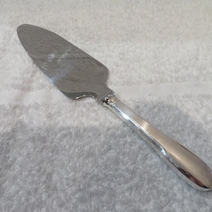 以下が含まれることがあります： 滑らかで丸みを帯びたハンドルとわずかにギザギザのエッジを持つ銀製のケーキサーバー