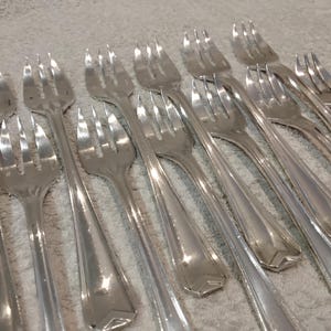 May include: A selection of polished silver forks, displayed at an angle. Each fork features four tines and a detailed handle. The cutlery is likely intended for use in a formal dining environment.