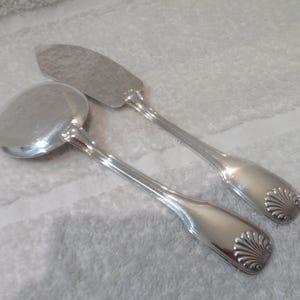 Puede incluir: Dos utensilios de servicio de plata, una cuchara y un cuchillo, con mangos ornamentados en forma de concha.