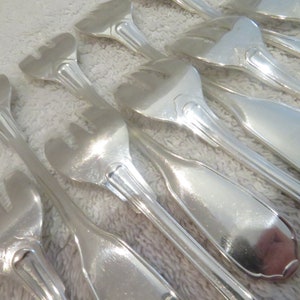 Pode incluir: Um conjunto de garfos de servir prateados com alças ornamentadas. Os garfos têm três dentes e estão dispostos em fila sobre uma superfície branca.