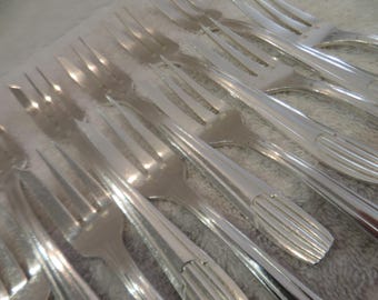 May include: A close-up of a set of silver forks, arranged in a row, with the tines facing up. The forks are shiny and reflect light.