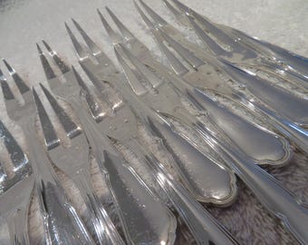May include: A close-up of several silver forks, each with multiple tines. The forks are arranged in a slightly overlapping pattern, reflecting light. The handles have a classic design. The image highlights the silverware's polished surface.