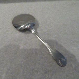 May include: A silver spoon with a rounded bowl and a decorative shell design on the handle.