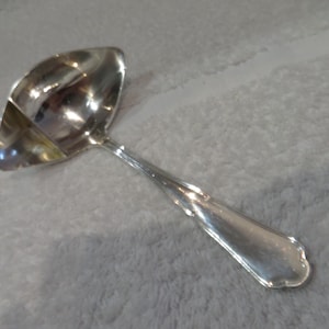 May include: A silver gravy ladle with a rounded bowl and a long, curved handle.