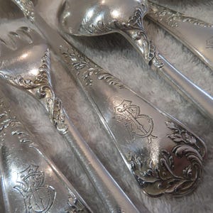 May include: A set of silver cutlery with ornate handles and engraved initials. The cutlery includes a fork, a spoon, and a knife.