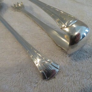 May include: A pair of silver-plated ice tongs with an ornate design. The tongs have a decorative handle with a monogram.