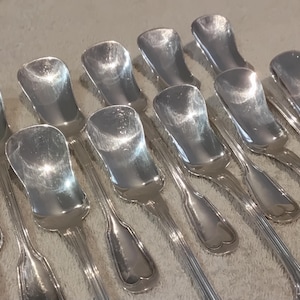 Puede incluir: Un conjunto de cucharas de servir plateadas con una forma de cuenco alargada distintiva. Las cucharas están dispuestas en un primer plano, mostrando sus superficies reflectantes y los detalles intrincados de los mangos. Probablemente para azúcar o condimentos.