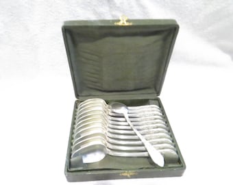 May include: A set of 12 silver spoons in a green velvet-lined box. The spoons are arranged in rows and are all the same size and shape.