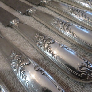 May include: A set of silver dinner knives with ornate floral designs on the handles.