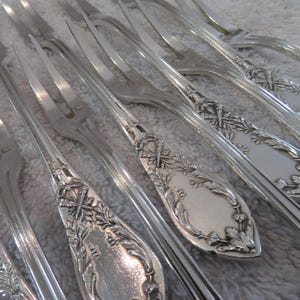 Peut inclure: Un ensemble de huit fourchettes en argent avec des manches ornés. Les manches présentent un motif floral avec une croix en haut.