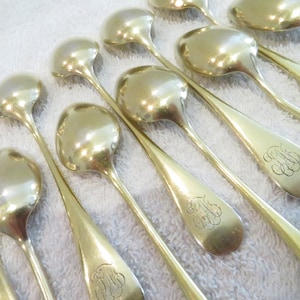 May include: A set of ten gold-plated spoons with ornate handles. Each spoon has a monogram engraved on the back of the handle.