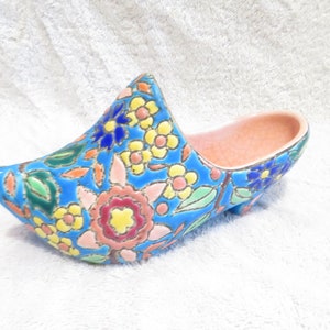 Könnte beinhalten: Ein blauer Keramikschuh mit Blumenmuster. Der Schuh hat ein rosafarbenes Innenleben und ist mit bunten Blumen und Blättern verziert.