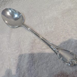 Peut inclure: Une cuillère en argent avec un bol arrondi et un long manche. Le manche présente des détails floraux ornés près de la base de la cuillère. La cuillère est probablement en acier inoxydable ou en métal similaire.