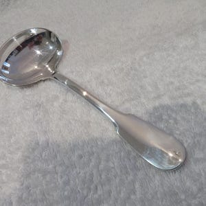 Può includere: Un cucchiaio da portata in argento con una ciotola arrotondata e un manico lungo e sottile.