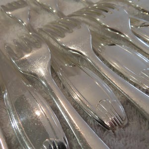 May include: A close-up of a set of silver forks, arranged in a fan shape. The forks are shiny and reflect light.