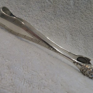 Peut inclure: Pinces à sucre en argent avec un motif décoratif de clé grecque et un motif de grappe de raisin sur les poignées.