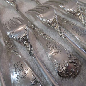 May include: A set of silver forks with ornate designs and intricate details. The forks are arranged in a fan shape, showcasing their elegant craftsmanship.
