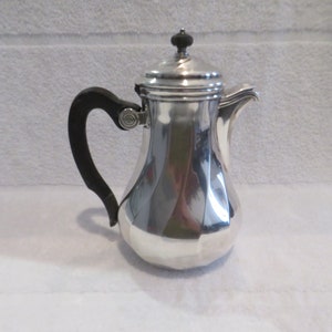 Op de afbeelding: Een zilveren theepot met een zwarte handgreep en een rond deksel. De theepot heeft een geribbeld ontwerp en is gepolijst.