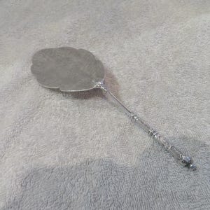 Puede incluir: Un servidor de pastel de plata con un mango adornado y una hoja en forma de hoja.