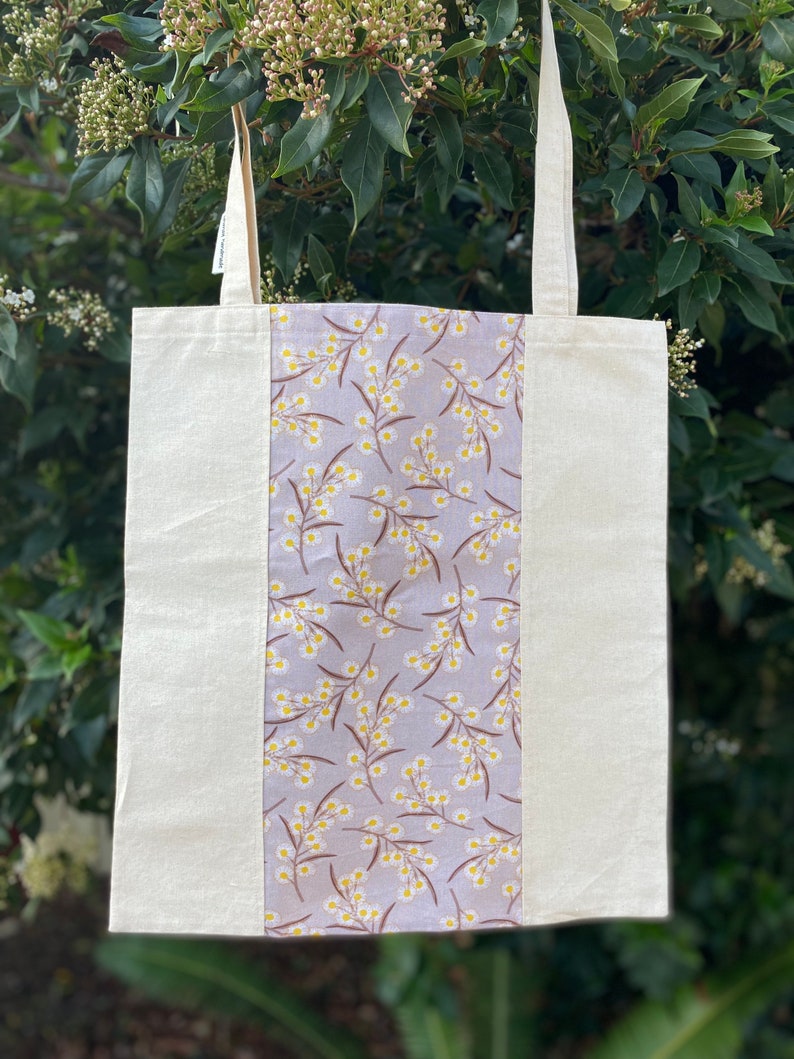 May include: A white tote bag with a grey and yellow floral print panel. The bag has two long straps.