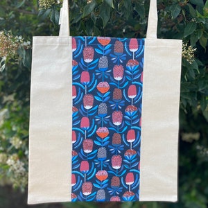 May include: A white canvas tote bag with a blue and pink floral pattern on one side. The floral pattern features stylized flowers with red centers and blue leaves.