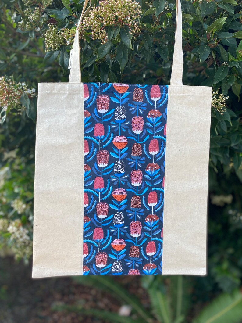 May include: A white canvas tote bag with a blue and pink floral pattern on one side. The floral pattern features stylized flowers with red centers and blue leaves.