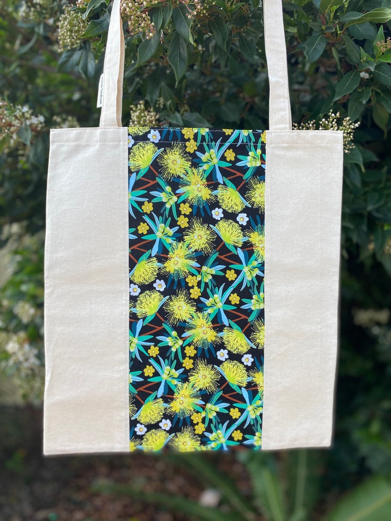 May include: A natural canvas tote bag with a black and yellow floral print panel. The print features yellow flowers with green leaves on a black background.