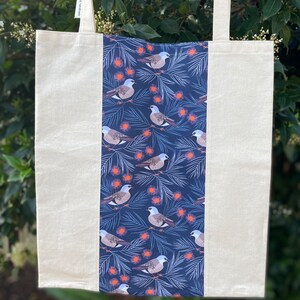 May include: A white canvas tote bag with a blue and white patterned panel featuring birds and flowers. The bag has two long straps.