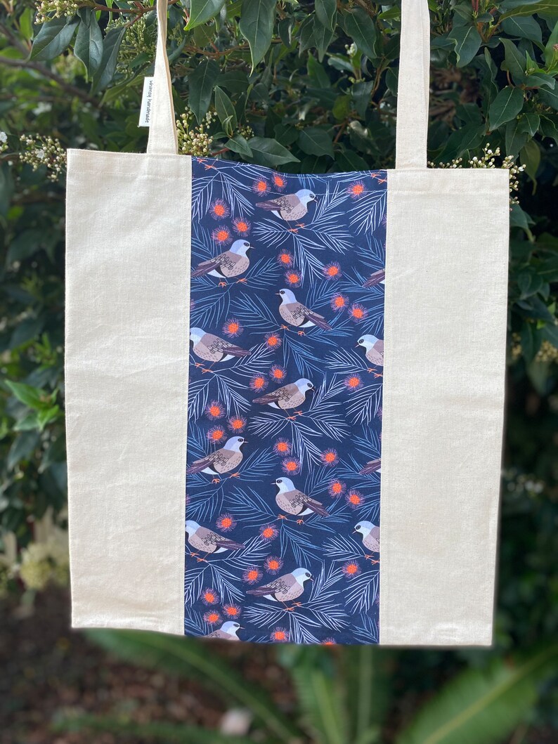 May include: A white canvas tote bag with a blue and white patterned panel featuring birds and flowers. The bag has two long straps.