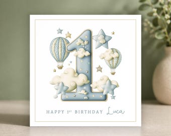Op de afbeelding: Vierkante verjaardagskaart met een lichtblauw cijfer één, wolken, sterren en luchtballonnen. De kaart leest "HAPPY 1ST BIRTHDAY Luca" in een handschrift. De kaart heeft een gouden rand en staat op een witte achtergrond.