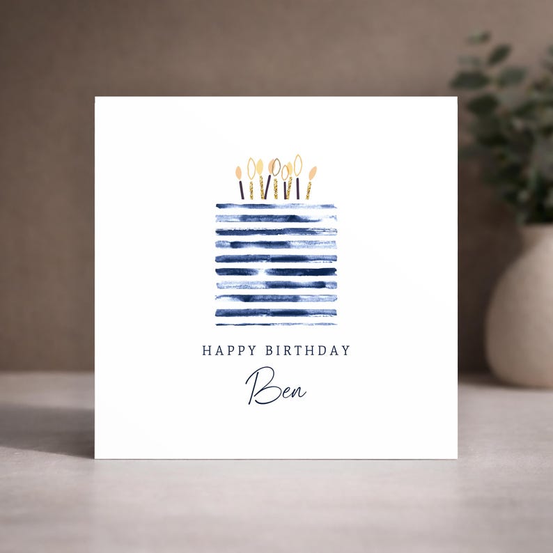 Puede incluir: Una tarjeta de felicitaci&oacute;n cuadrada de color blanco con una ilustraci&oacute;n en acuarela de un pastel hecho de rayas horizontales azul marino coronado con velas de purpurina dorada. El texto dice HAPPY BIRTHDAY y el nombre Ben en cursiva.