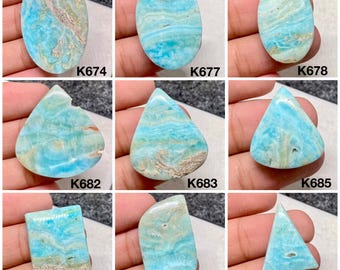 Peut inclure: Une collection de neuf pierres précieuses polies de formes variées, dont ovales, en forme de goutte et rectangulaires. Les pierres présentent une palette de couleurs bleu et beige frappante avec des motifs de veinage uniques. Chaque pierre est étiquetée avec un "K" suivi d'un numéro.