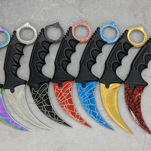 Peut inclure: Un ensemble de sept couteaux karambit incurvés avec des manches noirs texturés et des anneaux de doigt. Chaque lame présente une finition distincte, incluant des motifs arc-en-ciel, argentés, noirs, rouges, bleus, jaunes et en toile d'araignée.