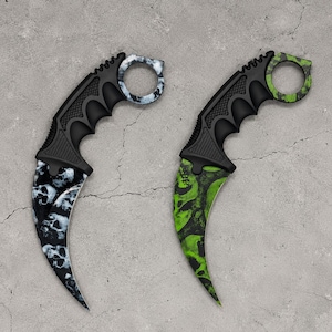 May include: Two karambit knives with curved blades and finger rings. One knife features a black and white skull pattern on the blade and ring, while the other displays a green and black skull pattern. Both have black textured handles.