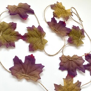 May include: A garland of faux fall leaves strung on twine. The leaves are a mix of purple, brown, and green.